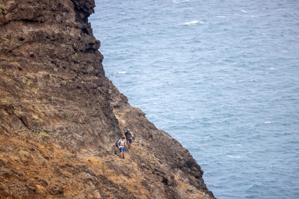 Two hikers crossing crawler's ledge on the Kalalau Trail.